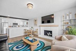 A modern living room with a fireplace, a dining area, and a kitchen in the background. - Spokane Apartment - North Atlantic Suite (Spokane)