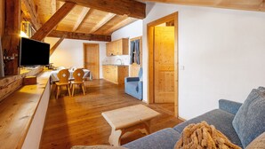 A wooden interior with a TV, wooden furniture, a sofa, and a kitchen area. - Apartment 'Plazores Dai Nüsc' with Mountain View, Shared Terrace and Wi-Fi (St. Vigil)