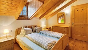 A wooden bedroom with a sloped ceiling, a bed with striped bedding, a nightstand, a dresser, and a door. - Apartment 'Plazores Dai Nüsc' with Mountain View, Shared Terrace and Wi-Fi (St. Vigil)