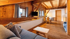 A cozy cabin interior with a wooden ceiling, a sofa, a table, and a TV. - Apartment 'Plazores Dai Nüsc' with Mountain View, Shared Terrace and Wi-Fi (St. Vigil)