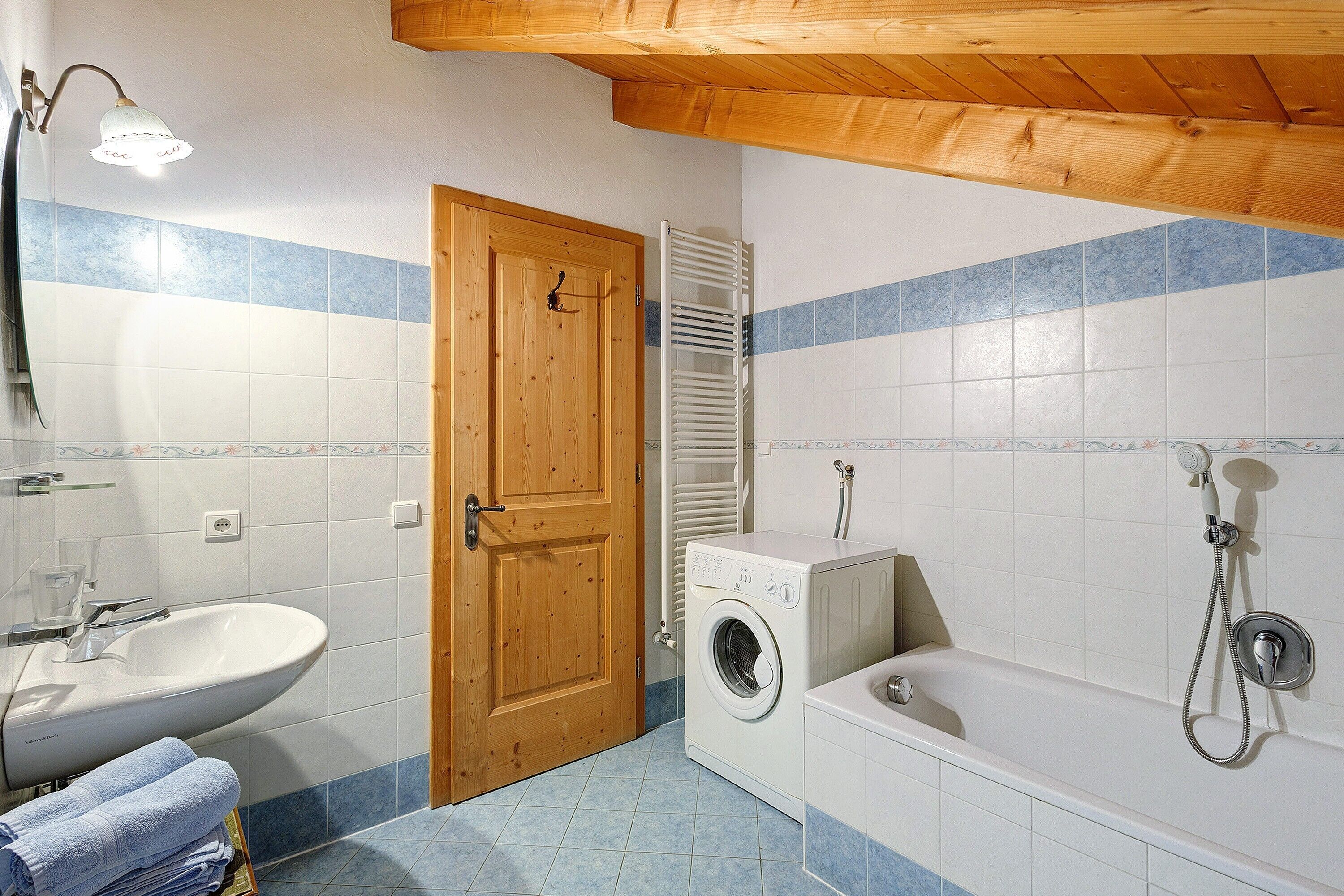 A bathroom with a sink, a washing machine, a bathtub, and a wooden door.