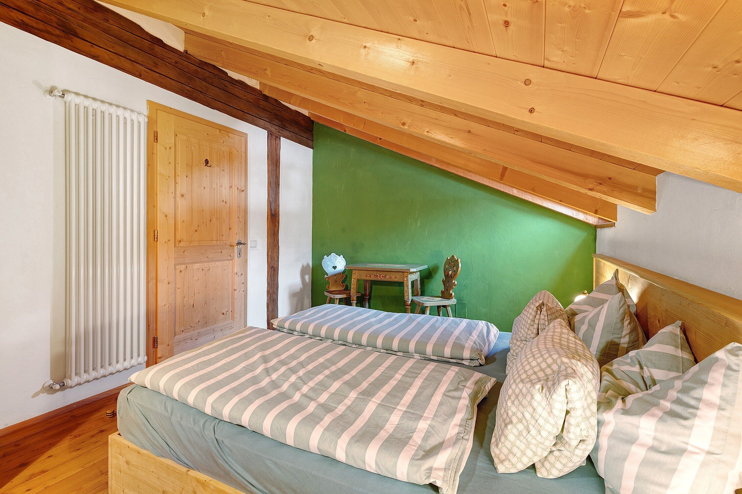 Ein Schlafzimmer mit Holzboden, grüner Wand, einem hölzernen Bett, einem Tisch aus Holz und einem Stuhl.