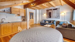 Un interior rústico con vigas de madera, una cocina con armarios de madera, una mesa redonda de comedor y un sofá.