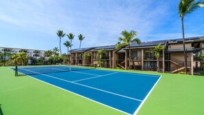 A tennis court with a net, surrounded by palm trees and a building with balconies. - Ocean View Top Floor Concierge Included! (Kailua-Kona)