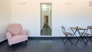 Une pièce avec un fauteuil rose, une table à manger avec des chaises et un couloir menant à une autre pièce.