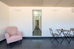Ein Zimmer mit einem rosafarbenen Sessel, einem Esstisch mit Stühlen und einem Gang zu einem anderen Raum.