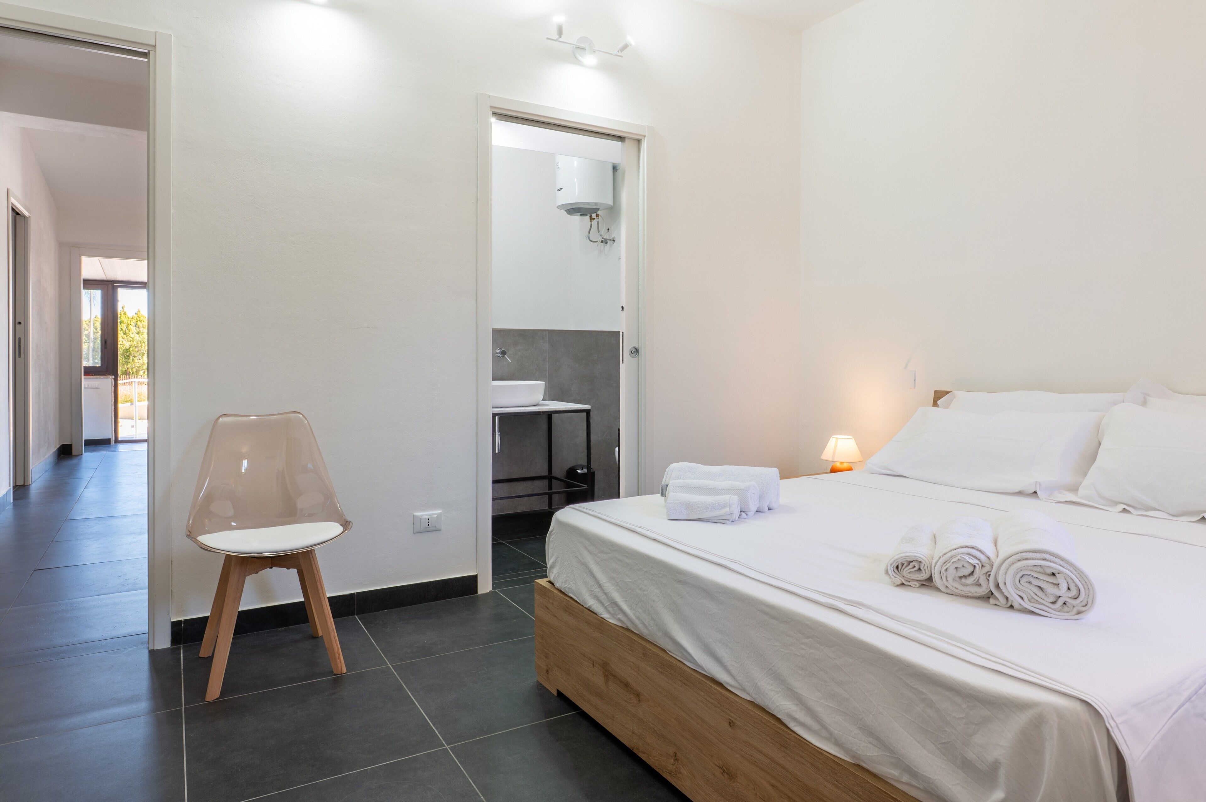 Una camera da letto con un letto, una sedia, un bagno e una porta che dà su un'altra stanza.