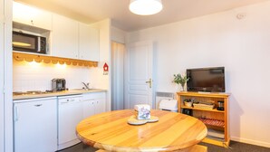 Una cocina compacta con gabinetes blancos, un microondas, una cafetera y una mesa con bancos.