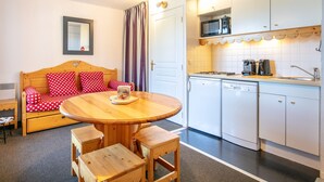 Una habitación acogedora con una cama de madera, una mesa de comedor y una zona de cocina con armarios y electrodomésticos blancos.