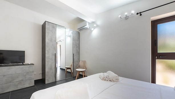 Een moderne hotelkamer met een bed, een televisie, een kledingkast, een spiegel en een raam.