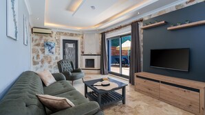 A modern living room with a sofa, armchair, and a flat-screen TV mounted on the wall. - Villa Elvin in Slamlar K y (Kaş)