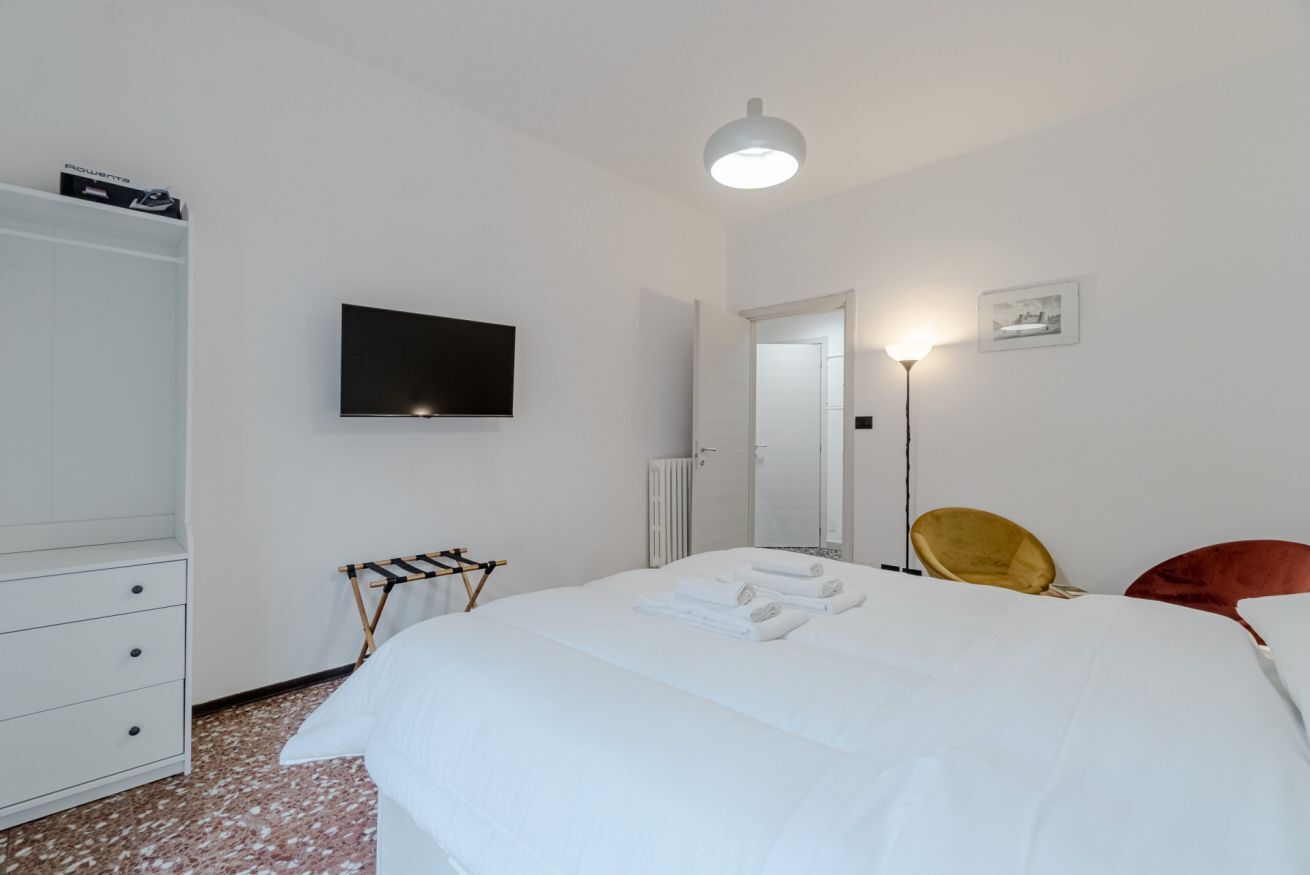 Ein Hotelzimmer mit Bett, Fernseher, Schrank, Heizkörper, Lampe und Stuhl.