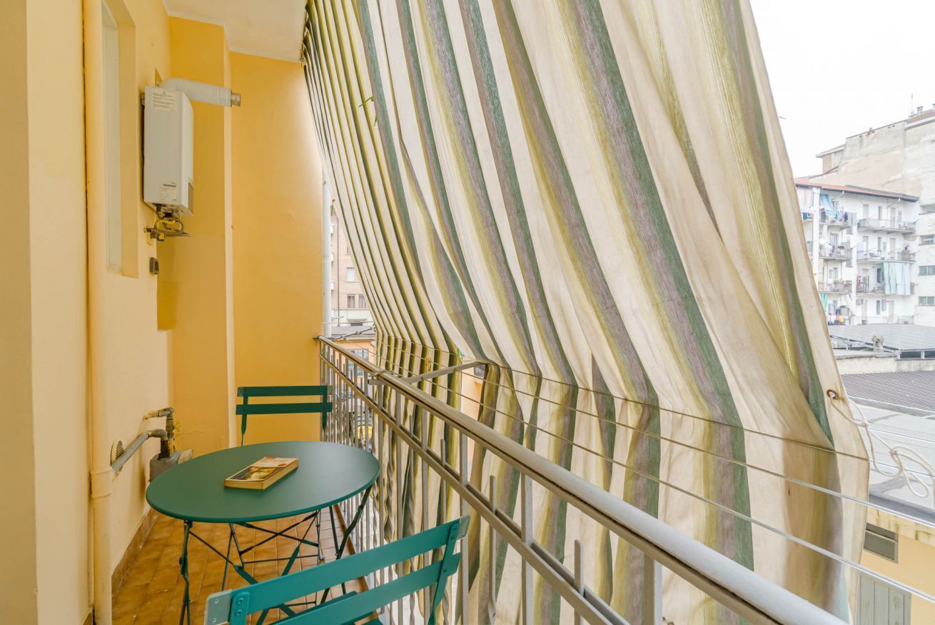 Un balcone con un tendaggio a righe, un tavolo con un libro e una sedia.