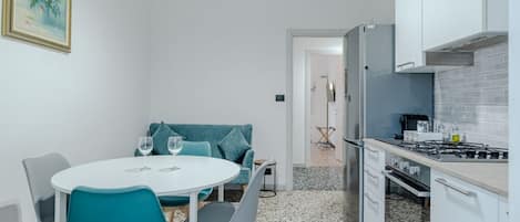 A compact kitchen with a gas stove, white cabinets, and a dining area with teal chairs and a white table.