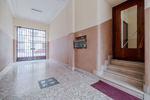 Un corridoio con pavimento piastrellato, una porta in legno e una scala.