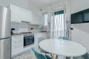 Cucina moderna con mobili bianchi, piano cottura e forno. C'è un tavolo da pranzo con sedie e un bicchiere da vino.