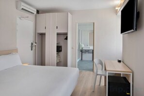 Una habitación de hotel con cama, escritorio, silla, televisor y armario.