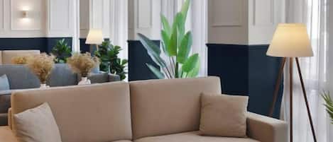 A beige sofa in a room with a large window, a floor lamp, and a plant.