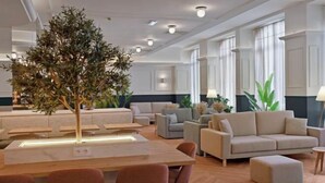 A spacious living area with a central table, multiple sofas, and a large artificial tree. - B&B HOTEL Figueira Da Foz (Figueira da Foz)