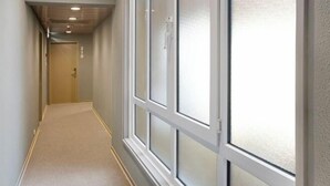 A hallway with a carpeted floor, a door at the end, and a window with frosted glass. - B&B HOTEL Figueira Da Foz (Figueira da Foz)