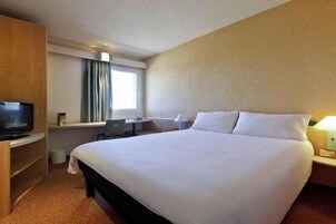 Una habitación de hotel con una cama grande, un escritorio con una silla, un televisor y una ventana con cortinas.
