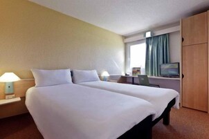 Habitación de hotel con dos camas, un escritorio, un televisor y un armario.