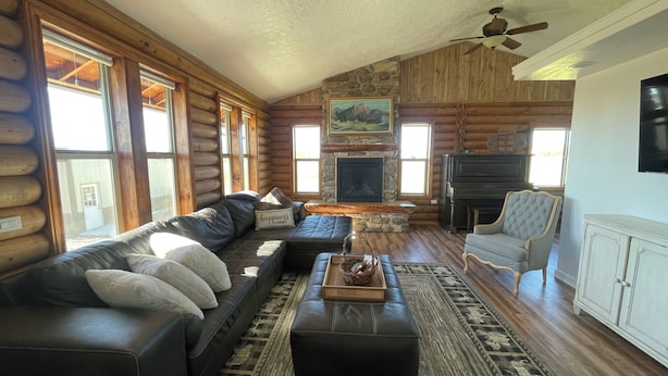 L’intérieur d’une cabane en rondins, avec une cheminée en pierre, un canapé en cuir et un téléviseur.