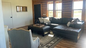 L’intérieur d’une cabane en rondins, avec un canapé d’angle, un fauteuil gris et un tapis à motifs.