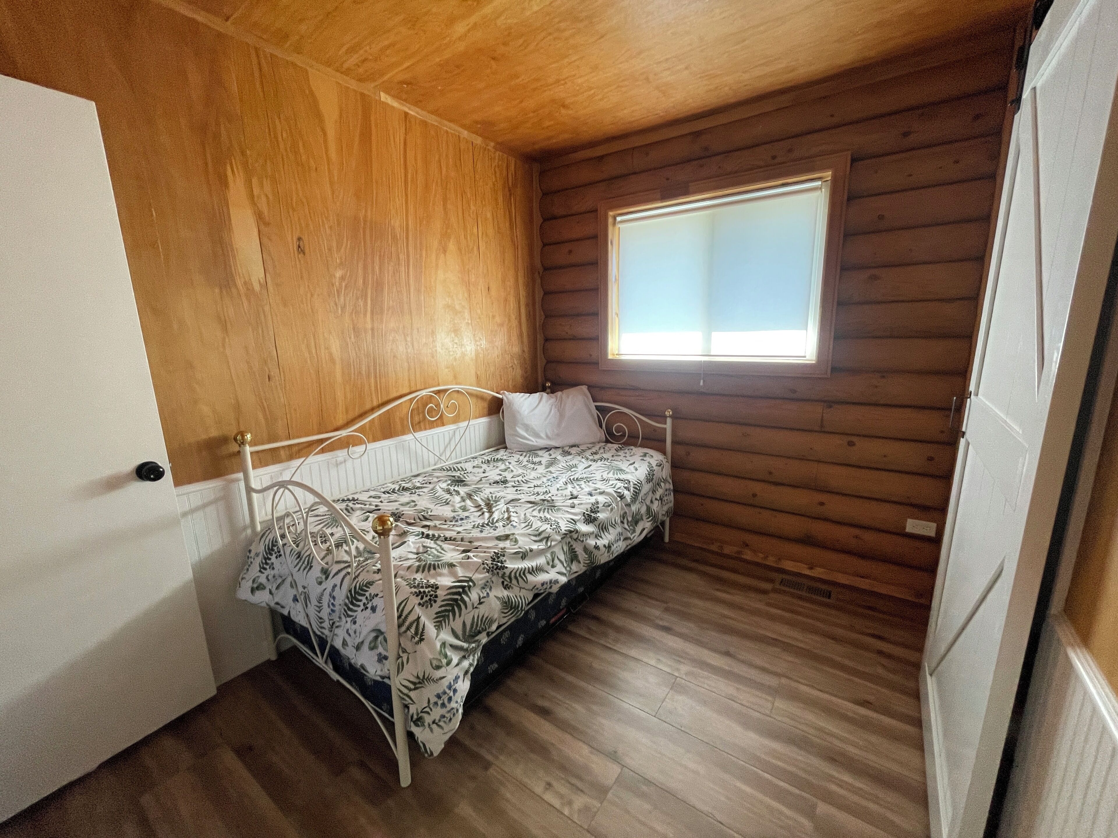 Een kleine eenpersoonskamer met houten wanden en een raam.