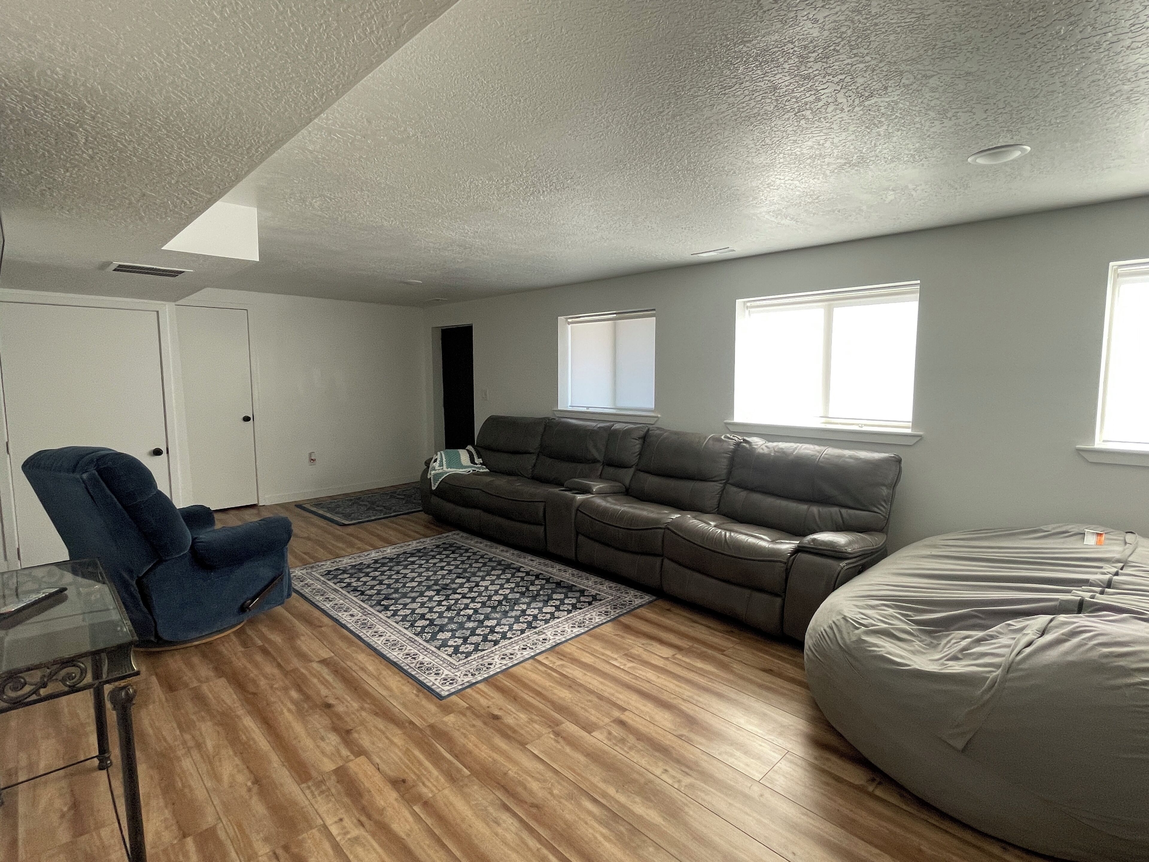 A living room with a brown leather sofa, a blue chair, a glass coffee table, and a beige bean bag.