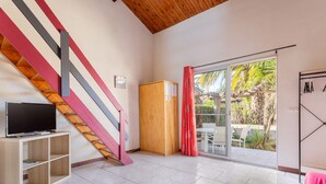 Une pièce avec un téléviseur posé sur un meuble en bois, un escalier avec des marches rouges et grises, un buffet en bois et une porte-fenêtre coulissante donnant sur un espace extérieur agrémenté de plantes.