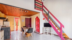 Un coin repas avec une table et des chaises, un espace cuisine avec un fourneau et un escalier doté d’une rampe rouge.