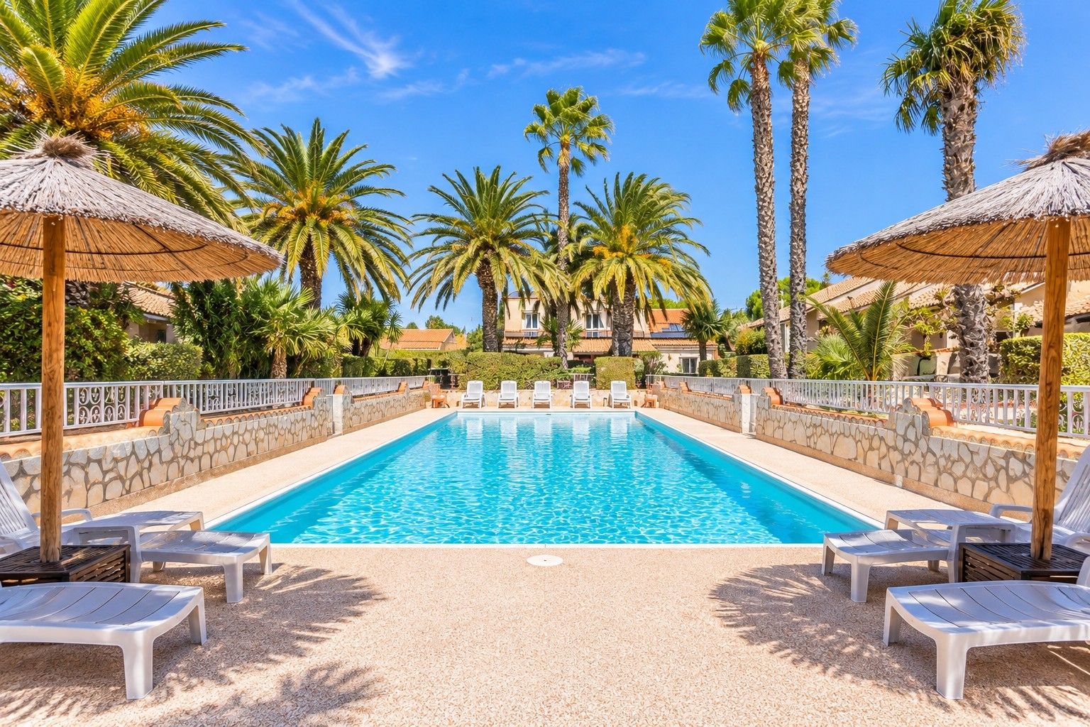 A swimming pool with lounge chairs and palm trees.