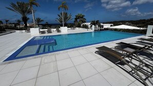 Ein Swimmingpool mit klarem, blauem Wasser, umgeben von Liegestühlen und Palmen.