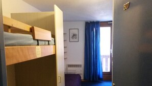 Una habitación con literas, una puerta con la etiqueta '507', una ventana con cortinas y un cuadro en la pared.