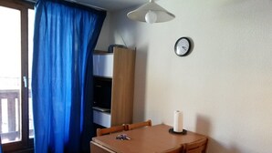 Una habitación con una mesa de madera, sillas, un reloj en la pared, una cortina azul y un ventilador de techo.
