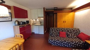 A compact living space with a kitchenette, a dining table, and a patterned sofa. - Bright studio with balcony and mountain view (Saint-Chaffrey)