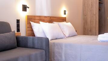 Un dormitorio moderno con cabecera de madera, ropa de cama blanca y un sofá gris.