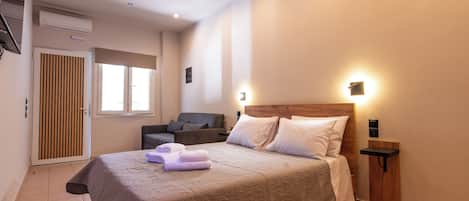 A bedroom with a large bed, a bedside table, a wall-mounted light, a window, a door, and a ceiling fan.