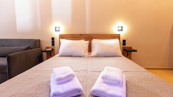A neatly made bed with two pillows, a bedside table with a lamp, and a couch in a hotel room.