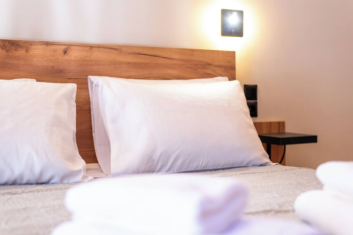 A neatly made bed with white linens and a wooden headboard.
