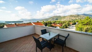 Un balcon avec une table et des chaises, donnant sur un paysage magnifique avec des montagnes et une étendue d’eau.
