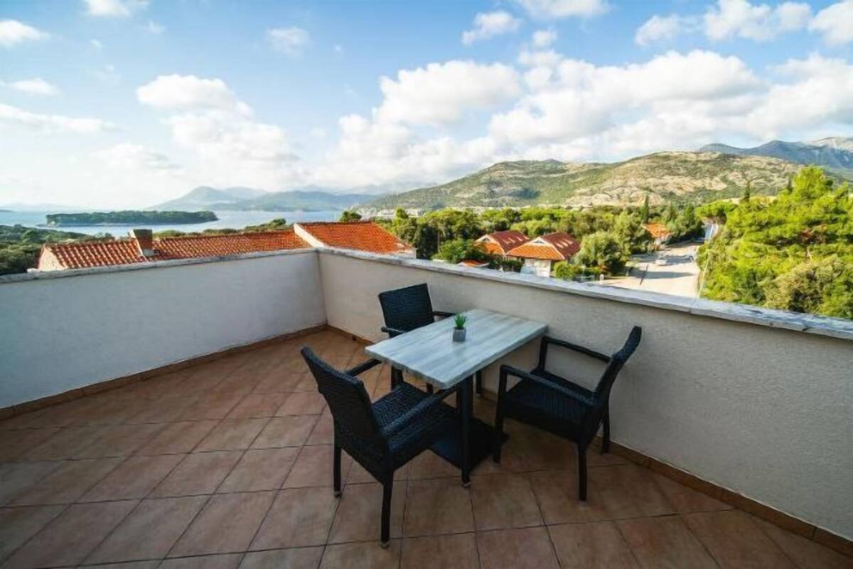 Un balcón con mesa y sillas, con vistas a un paisaje pintoresco con montañas y una masa de agua.