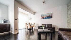 Un salon moderne avec un sol carrelé foncé, un canapé en cuir marron, un coin repas avec des chaises en bois et un tableau accroché au mur.