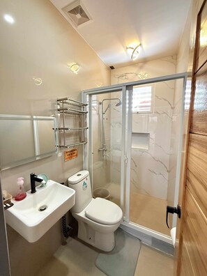 A modern bathroom with a glass-enclosed shower, a white sink with a soap dispenser, and a toilet.