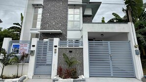 A modern two-story house with a large garage door, a balcony, and a sign indicating it is for sale.