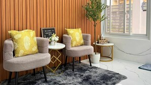 A modern living room with two grey armchairs, a black and white rug, a wooden wall, a small table with a plant, and a window with a view of the outside.