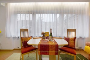 Un área de comedor con una mesa, sillas y un ventanal con cortinas translúcidas.