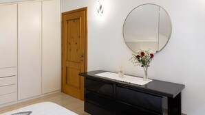 Quarto com guarda-roupa, mesa de cabeceira com espelho e um vaso com flores.