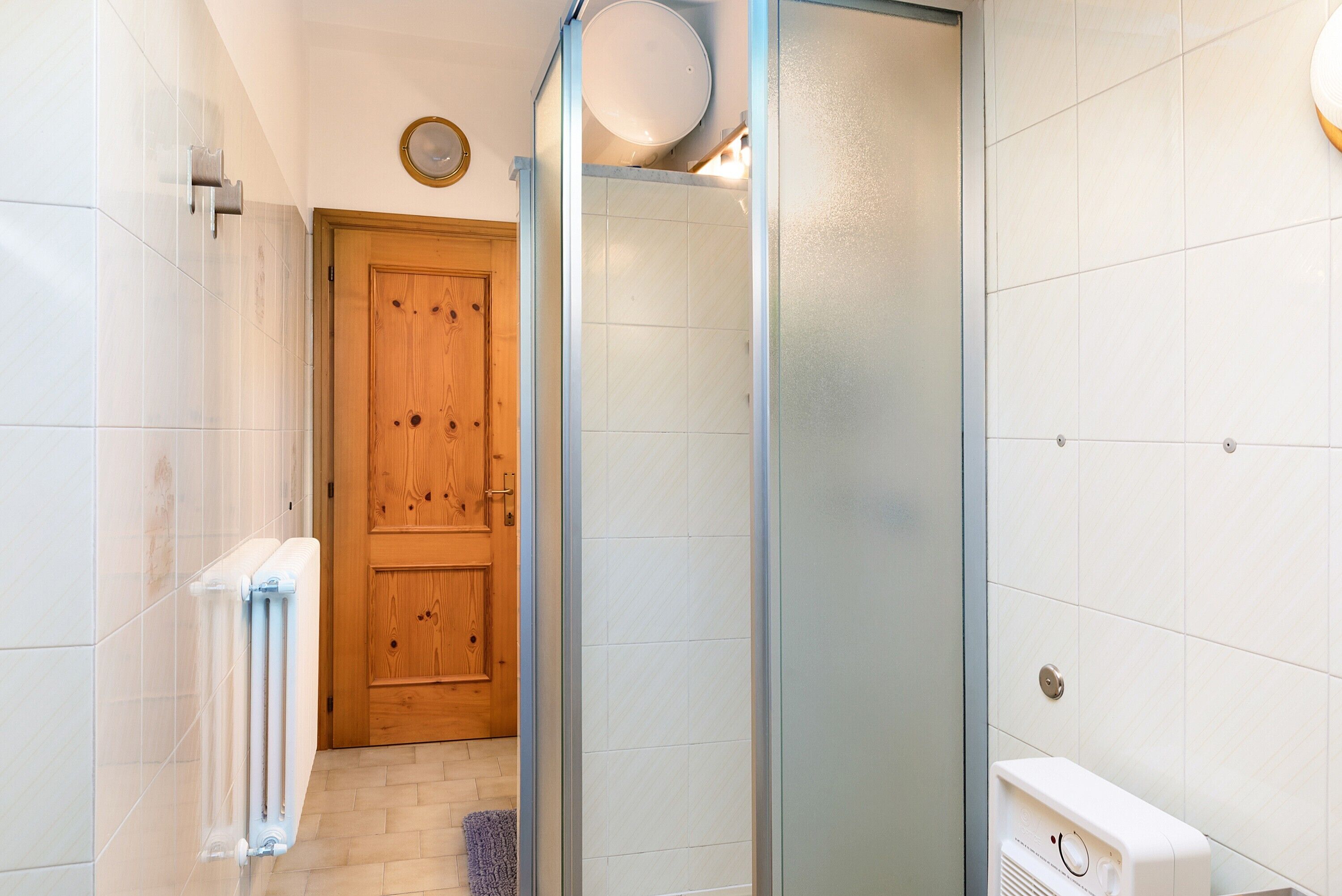 Een badkamer met een houten deur, een douchecabine van glas, een witte radiator en een toilet.